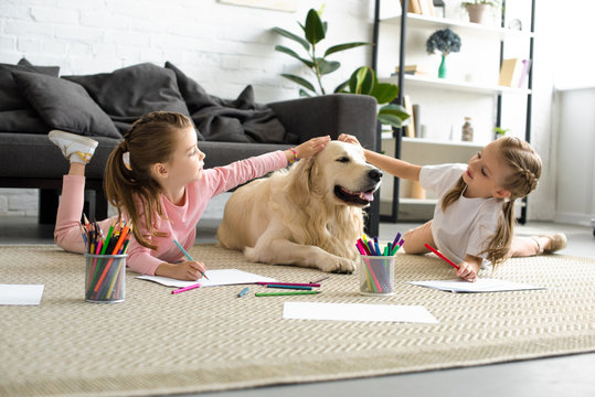 adorable kids petting golden retriever dog while drawing pictures on floor at home