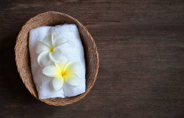 White flower decorate on towel which carry on basket on wood table, spa concept.