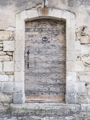 very old thick wooden medieval door in ancient limestone wall in village of french provence