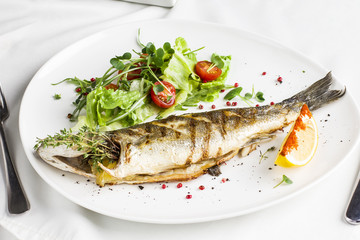 Baked fish with lemon and fresh vegetables on a white plate in the restaurant