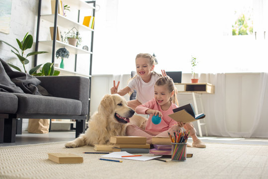 little sisters with books and golden retriever dog near by playing together at home
