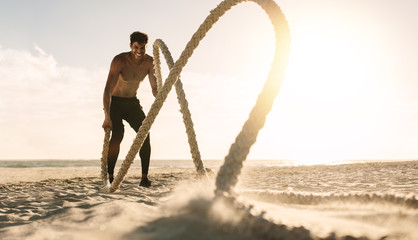 Man doing workout using battling ropes at the beach