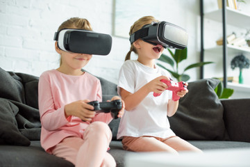 little kids in virtual reality headsets playing video game on sofa at home