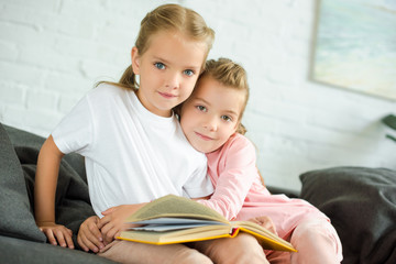Fototapeta premium portrait of little child hugging sister with book on sofa at home
