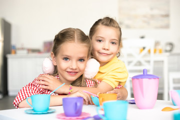 portrait of little smiling sisters pretending to have tea party together at home