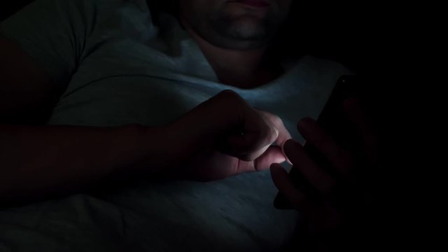 Man in bed reading news on a smartphone. Night.