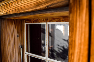 Beautiful close-up view of an old, weathered wooden window with a big window frame seen at a mountain cabin in the Swiss Alps, Switzerland. Snow is reflected in the window glass.