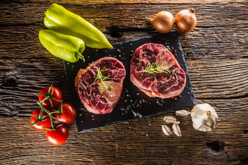 Two pieces raw beef shank and basic ingredients on goulash - onion pepper tomatoes garlic salt...