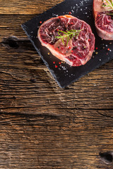 Two pieces raw beef shank on slate board and wooden table.