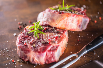 Two raw pieces beef shank on wooden butcher board with fork and knife.