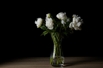 beautiful white peonies in glass vase on wooden table and on black