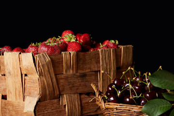 Obraz na płótnie Canvas ripe cherries and strawberries in basket and box isolated on black