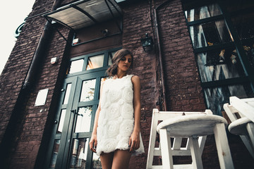 A girl in a white dress and white sneakers.Beautiful brunette in white dress.Girl near big Windows