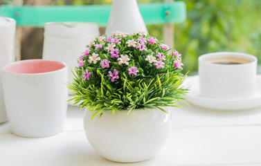 Plastic flower bouquet  in a pot placed on a white wooden log in the garden.