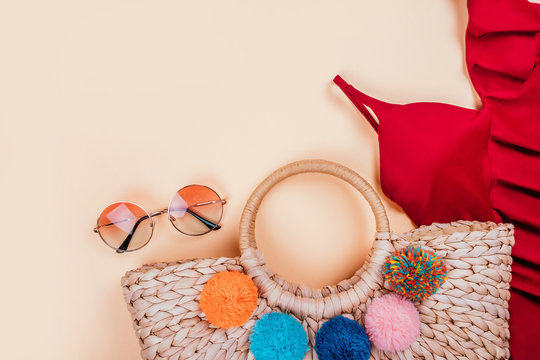 Summer Fashion Flatlay With Gradient Round Sunglasses, Trendy Straw Bag With Pompoms And Red Swimsuit With Frills On The Beige Background. Perfect Beach Set For Holidays On The Sea. Marina Style.