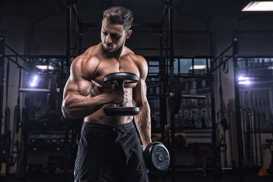 Fototapeta Young handsome sportsman bodybuilder weightlifter with an ideal body, after coaching poses in front of the camera, abdominal muscles, biceps triceps. In sportswear.