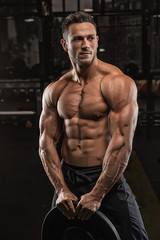 Fototapeta na wymiar Young handsome sportsman bodybuilder weightlifter with an ideal body, after coaching poses in front of the camera, abdominal muscles, biceps triceps. In sportswear.