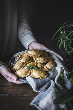 Close up of woman's hands holding baked empanada served on a plate