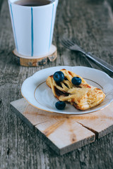 Puff pastry with jam and blueberries in a white plate on a wooden background, cup of coffee, breakfast