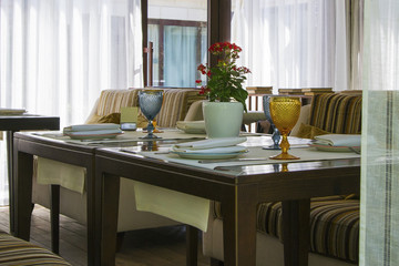 Modern european restaurant with wooden table and multi-colored sofa close to window.  Table setting.