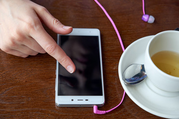 Woman hands with smart phone, headphones and cup of tea. For Graphic display montage.