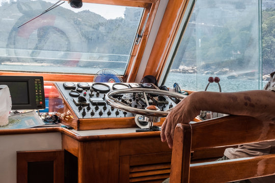 Navigation console with metal steering wheel inside the motorboat deck house. Boat driver sitting near the wheel. Dirty windows splashing with sea water. 