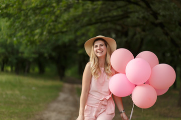 Woman with a wicker basket, hat, pink ballons and flowers walking on a country road