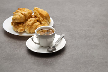 Cup of fresh coffee with croissants on dark background