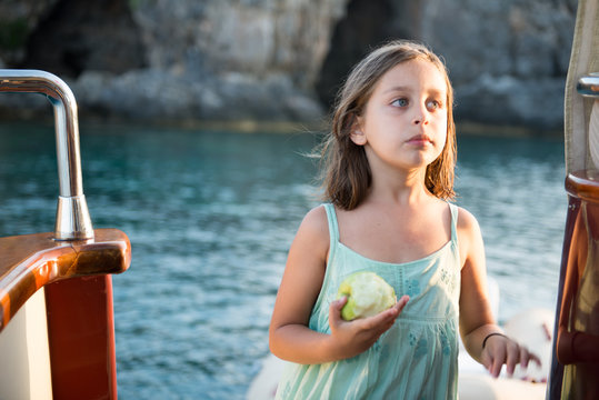 cute girl is eating her apple on the boat