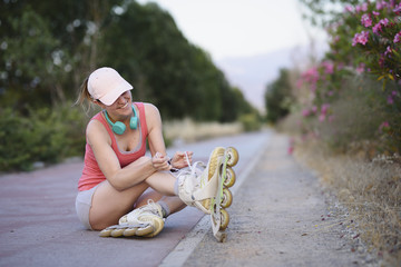 Young sportswoman with cap and headphones tightening up her roller skates