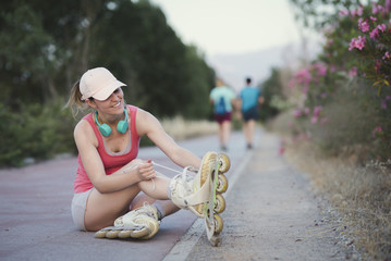 Young sportswoman with cap and headphones tightening up her roller skates