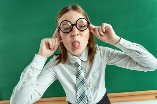 Naughty pupil making sassy funny expressions, showing her tongue / photo of teen school girl wearing glasses, creative concept with Back to school theme