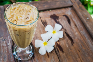 A coffee glass in the garden with white plumeria flowers on wooden floor.