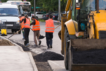 Workers in overalls laid asphalt along the curb on the roadway