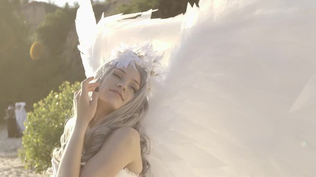 Delicate beautiful blonde woman posing with angel wings seashore
