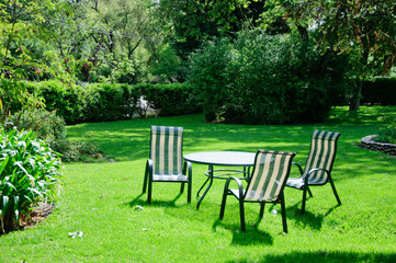 Green summer backyard garden with grass, table and chairs