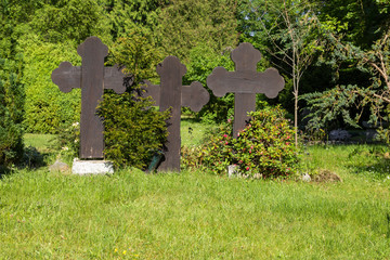 Drei große Kreuze mit Büschen und Bäumen auf einem Friedhof