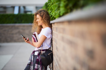 Fototapeta na wymiar Female student using smart phone and holding books while walking in campus.