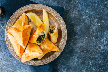 Arabic and middle eastern food concept. Fatayer sabanekh - traditional arabic spinach triangle hand pies on a blue stone background. - 210299268
