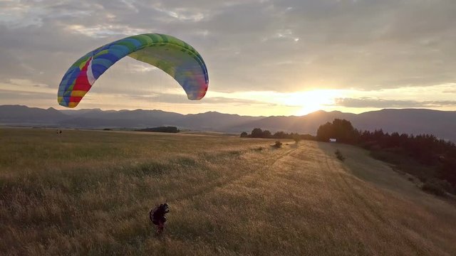 Playing with paraglider in golden meadow at sunset