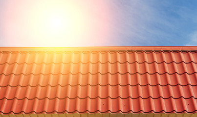 View of red roof tiles and sky with sun.