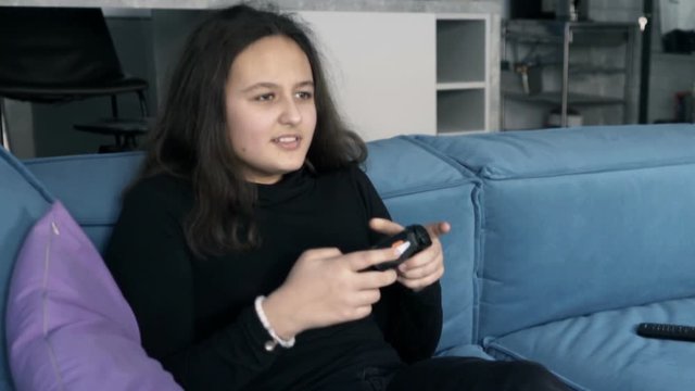 Teenage girl looses while playing game on play station on sofa at home
