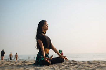 Young healthy woman practicing yoga on the beach at sunset