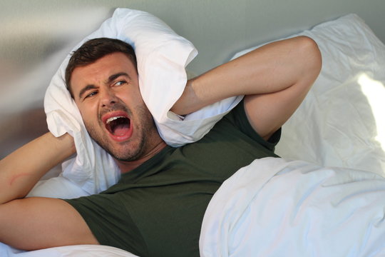 Man screaming at home while covering ears 