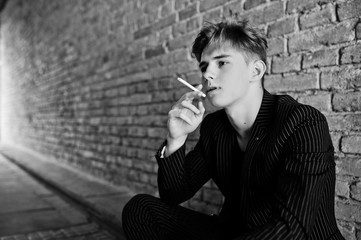 Young macho boy wear on blac stylish jacket smoking cigarette on streets.