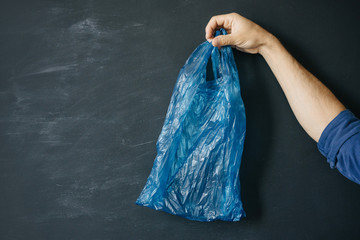 Plastic disposable blue shopping bag in man's hand on a dark background. The problem of plastic packaging and environmental protection.