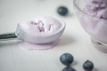 Melted blueberry ice cream in a spoon on white wooden table with berries. Shallow depth of field. Close-up..