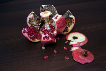 Rotten, spoiled, polished red pomegranate on a wooden table with seeds.