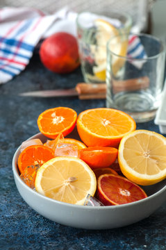 Mix of fresh ripe citrus fruits as blood oranges, mandarines, lemons  with ice cubes in a bowl on a blue stone background.