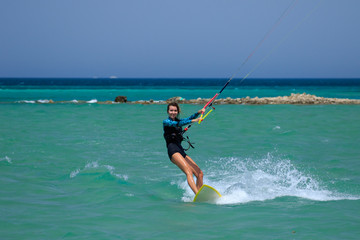 Kite surfing girl in sexy swimsuit with kite in sky on board in blue sea riding waves with water splash. Recreational activity, water sports, action, hobby and fun in summer time. Kiteboarding sport
